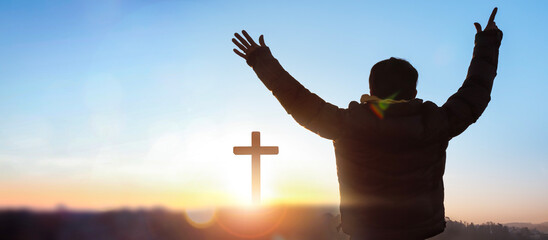 Silhouette of a man praying before a cross at sunrise background.
