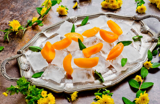 Antigua bandeja de metal con cubitos de hielo, trozos de melocot&oacute;n y crisantemos amarillos