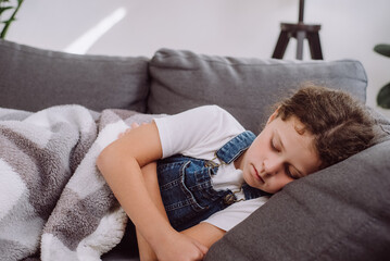 Close up of sick unhealthy preteen girl lying alone on sofa under blanket in living room at home. Ill upset caucasian child has fever. Concept of health, illness, sickness, common cold, treatment - obrazy, fototapety, plakaty