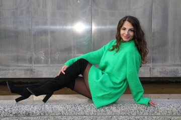 Portrait of an attractive pretty woman in green mini dress, sitting against a silver background
