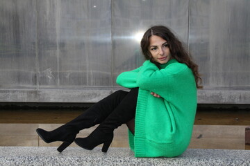 Portrait of an attractive pretty woman in green mini dress, sitting against a silver background