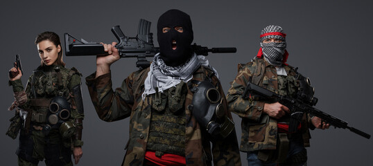 Group of three Middle Eastern militants dressed in camouflage uniforms, keffiyehs, and balaclavas posing against a gray background