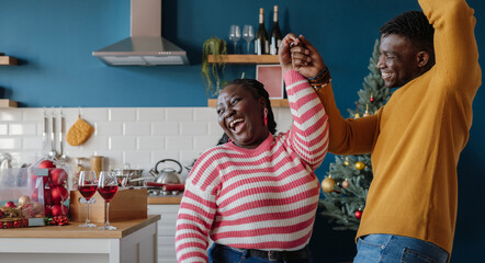 Joyful young African couple dancing and smiling while celebrating New Year at home together