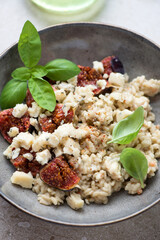 Close-up of risotto with torn fig fruits, blue cheese and fresh basil served in a grey plate, vertical shot, selective focus