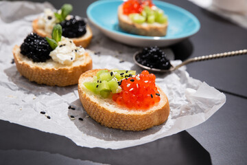Fusion cuisine concept. Fine dining with caviar appetizer. Fine dining with caviar appetizer, red and black caviar canape of white crispy baguette bread with chopped kiwi fruit and sezame seeds. 