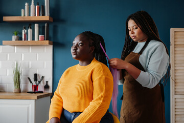 Confident African American hairdresser braiding hair to a female customer in salon - obrazy, fototapety, plakaty