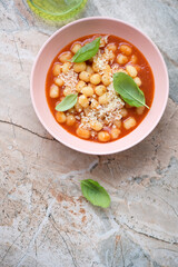 Roseate bowl with tomato gnocchi soup on a pinkish granite background, vertical shot with space, top view
