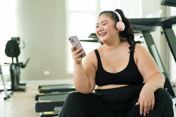 Chubby woman sits with headphones on. Listen to music in the fitness center Happiness of a cute...