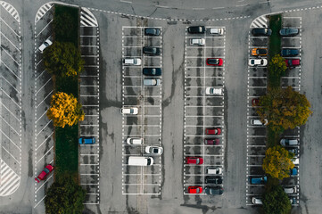 Parking lot and parked colorful cars between the lines from above (top view) - grey concrete background. Parking lot with colorful trees in autumn season.