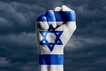 Man hand fist of ISRAEI flag painted. Against the background of dark clouds.
