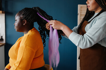 Close-up of confident hairdresser braiding hair to a young African woman in salon - obrazy, fototapety, plakaty