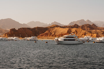 Sea ​​coast with yachts and deserted Egyptian mountains in the background. Seascape in hot summer. Seascape photo in cinematic warm colors.