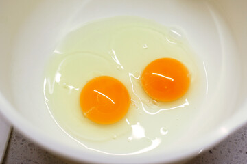 Cooking at home. High angle view of two egg yolks and whites in ceramic bowl