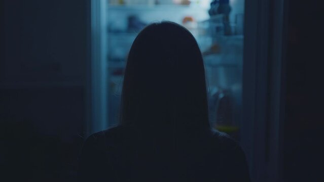 Woman opens fridge looking for snack in kitchen at night