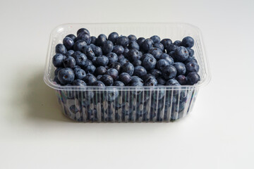 Fresh juicy blueberries and blueberries in a transparent plastic container on a white table
