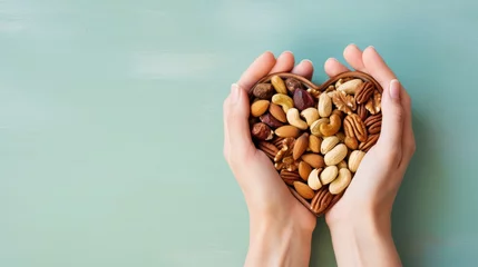 Fotobehang  two hands holding a heart shaped basket filled with nuts on a blue and green background with space for a text or a picture of a hand holding a heart shaped basket filled with nuts. © Olga