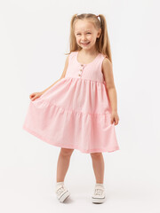 A cute 5-year-old girl with long hair stands on a white background smiling, straightens her pink...