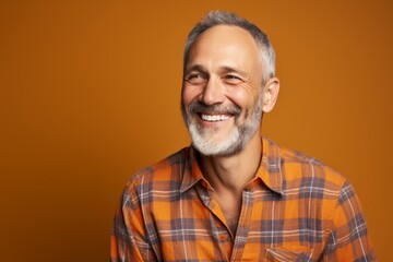 Obraz premium Portrait of a grinning man in his 50s dressed in a relaxed flannel shirt against a pastel orange background. AI Generation
