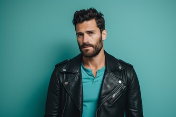 Fototapeta premium Portrait of a blissful man in his 30s sporting a classic leather jacket against a pastel teal background. AI Generation