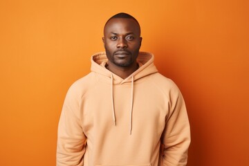 Obraz premium Portrait of a tender man in his 40s sporting a comfortable hoodie against a soft orange background. AI Generation