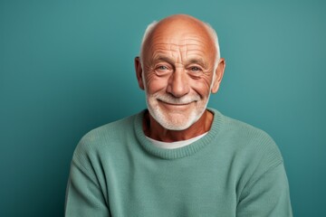 Portrait of a grinning man in his 70s dressed in a comfy fleece pullover against a soft teal background. AI Generation