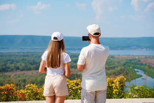 People a man and a girl, or a father and a teenage daughter take pictures of a stunning panorama of the Volga River on a summer day. Beautiful landscape in Russia. Togliatti, Russia - August 28, 2023