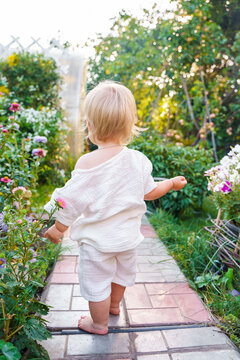 Little child baby in a muslin white suit in the garden at the dacha in summer, happy active summer