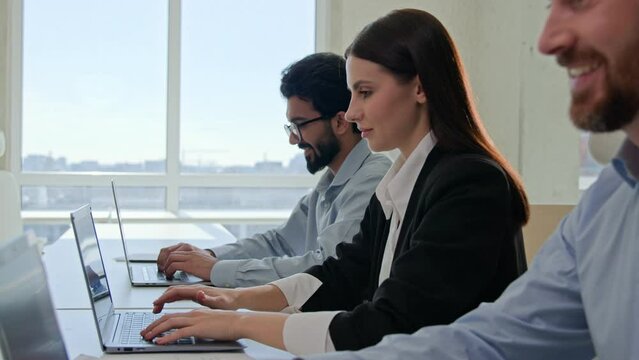 Row of multiracial customer support agents provide service with laptops smiling professional business team programmers businessmen and businesswoman working desktop pc computers at co-working office