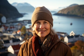 Portrait of a glad woman in her 50s dressed in a warm ski hat against a beautiful coastal village background. AI Generation