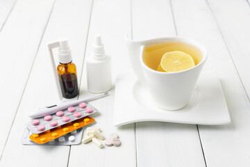 Tea cup with lemon, cold remedies, medicine, thermometer, capsules and pills in a blister pack on wooden table. Concept of home treatment flu and coronavirus