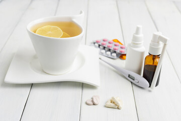 Tea cup with lemon, cold remedies, medicine, thermometer, capsules and pills in a blister pack on wooden table. Concept of home treatment flu and coronavirus