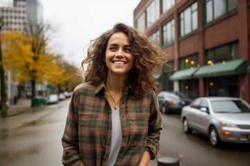 Obraz premium Portrait of a cheerful woman in her 30s wearing a comfy flannel shirt against a bustling city street background. AI Generation