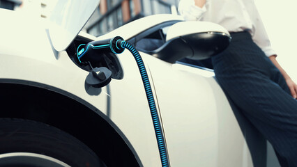 Businesswoman waiting after recharge electric car from charging station at city center or public...