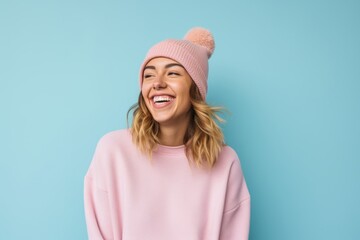 Portrait of a happy woman in her 20s donning a warm wool beanie against a pastel or soft colors...