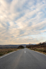 New country road in autumn.  Country road cutting through green fields in the countryside. Empty asphalt road in rural landscape with dramatic clouds. Open Road.  