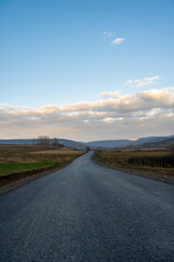 New country road in autumn.  Country road cutting through green fields in the countryside. Empty asphalt road in rural landscape with dramatic clouds. Open Road.  