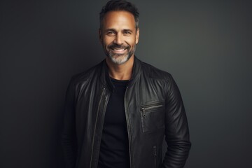 Fototapeta premium Portrait of a happy man in his 40s sporting a classic leather jacket against a minimalist or empty room background. AI Generation