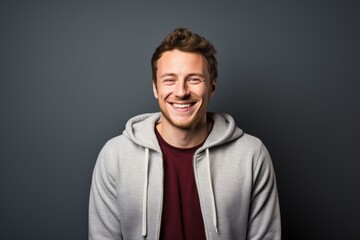 Fototapeta premium Portrait of a grinning man in his 20s wearing a zip-up fleece hoodie against a minimalist or empty room background. AI Generation