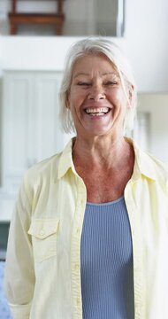 Happy caucasian senior woman standing and laughing in sunny room, slow motion