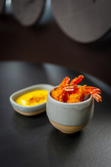 Tempura deep-fried shrimp with spiced sauce on a plate on a dark background.