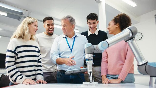 Camera pulls back from multi-cultural group of university or college students in STEM or engineering class with male tutor demonstrating robotic arm - shot in slow motion