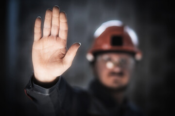 A miner or worker in overalls and a hard hat shows an open palm, a crisis in the workplace, a...