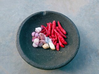 various cooking spices (red chilies, onions, garlic, candlenuts and salt) in a mortar to make chili...