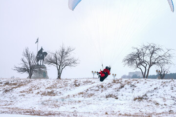 Winter paragliding. Jump from the mountain. Pilot in a capsule on slings in the air. Copy space.