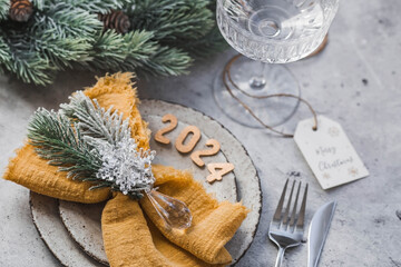 Obraz na płótnie Canvas Table setting. Stylish plates, napkin, glass, champagne, Christmas tree branches and Christmas decorations on a gray background. The concept of merry Christmas and New Year 2024.