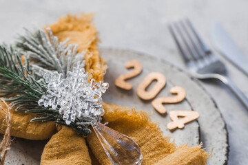 Table setting. Stylish plates, napkin, glass, champagne, Christmas tree branches and Christmas decorations on a gray background. The concept of merry Christmas and New Year 2024.