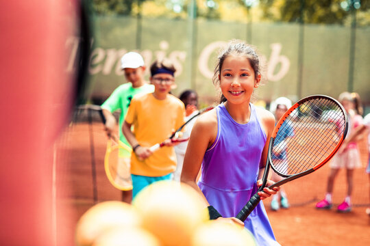 Young girl with a smile holding a tennis racket among other junior players