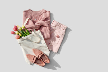 Fashion spring outfit. Pale pink jumper with bouquet of tulips flowers in bag,  jeans and loafers. Women's stylish and elegant clothes with accessory and jewelry.  Flat lay, top view, overhead. - obrazy, fototapety, plakaty