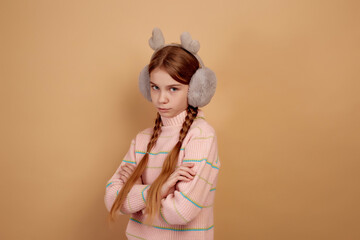 Little offended girl with fluffy headphones on beige background.