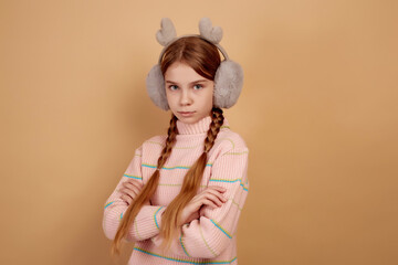 Little offended girl with fluffy headphones on beige background.